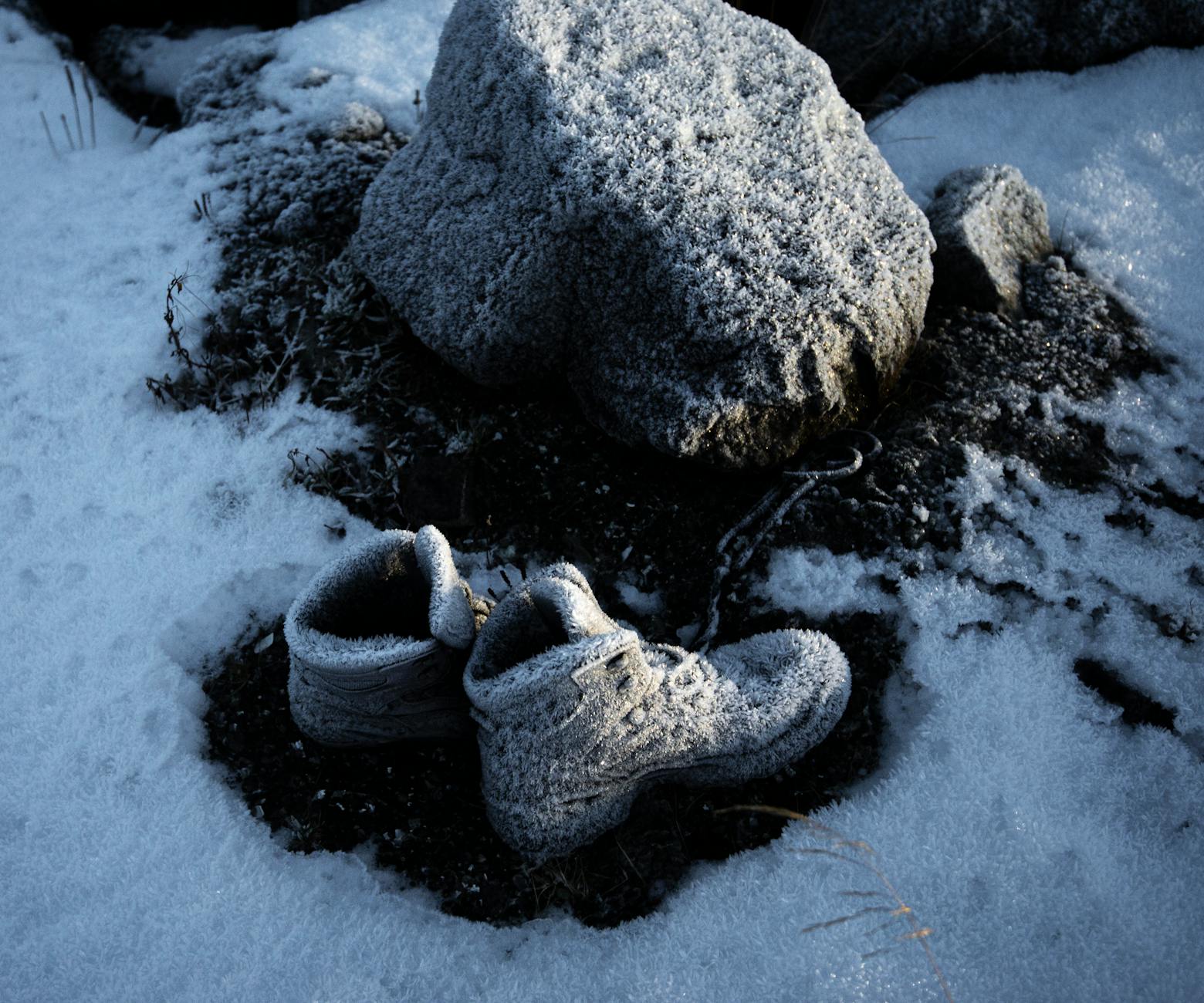 Zbliżenie zamarzniętych butów trekkingowych na ośnieżonych skałach